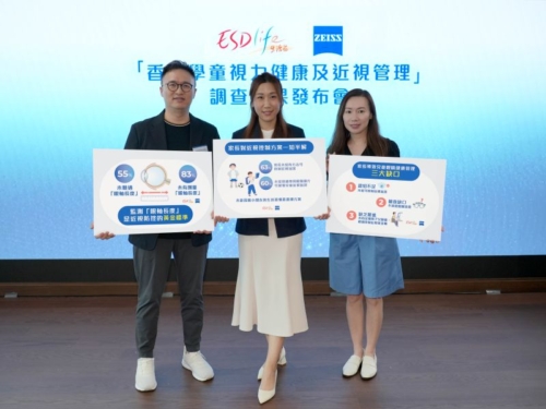  Three people standing on a stage holding informational signs during a press conference about children's vision health and myopia management, with a backdrop featuring the logos of ESDlife and ZEISS. 