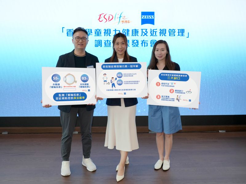 Three people standing on a stage holding informational signs during a press conference about children's vision health and myopia management, with a backdrop featuring the logos of ESDlife and ZEISS.